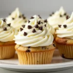 Frosted chocolate chip cupcakes topped with mini chocolate chips on a white plate.