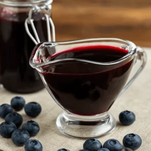 Glass sauce boat filled with rich blueberry syrup, surrounded by fresh blueberries — a finished look at the blueberry syrup recipe.