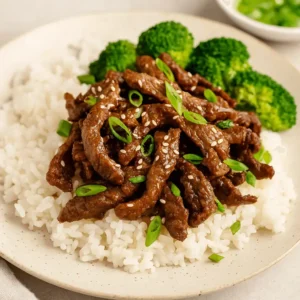 Shaved beef recipe served over steamed white rice with broccoli and sesame seed garnish.
