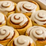 Freshly baked cinnamon rolls in a white dish topped with creamy glaze from a cinnamon roll icing recipe
