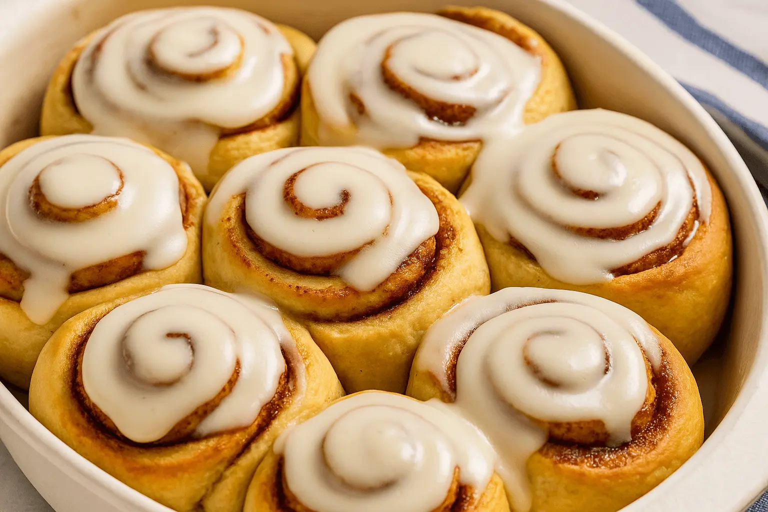 Freshly baked cinnamon rolls in a white dish topped with creamy glaze from a cinnamon roll icing recipe