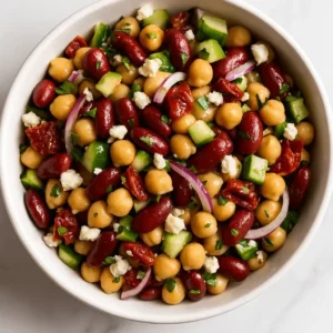 Overhead view of dense bean salad with chickpeas, kidney beans, cucumbers, red onion, sun-dried tomatoes, and feta.