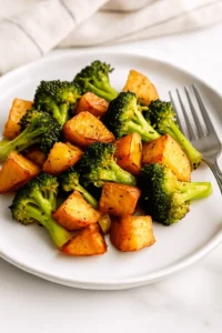 Roasted potatoes and broccoli served on a white plate with a fork.