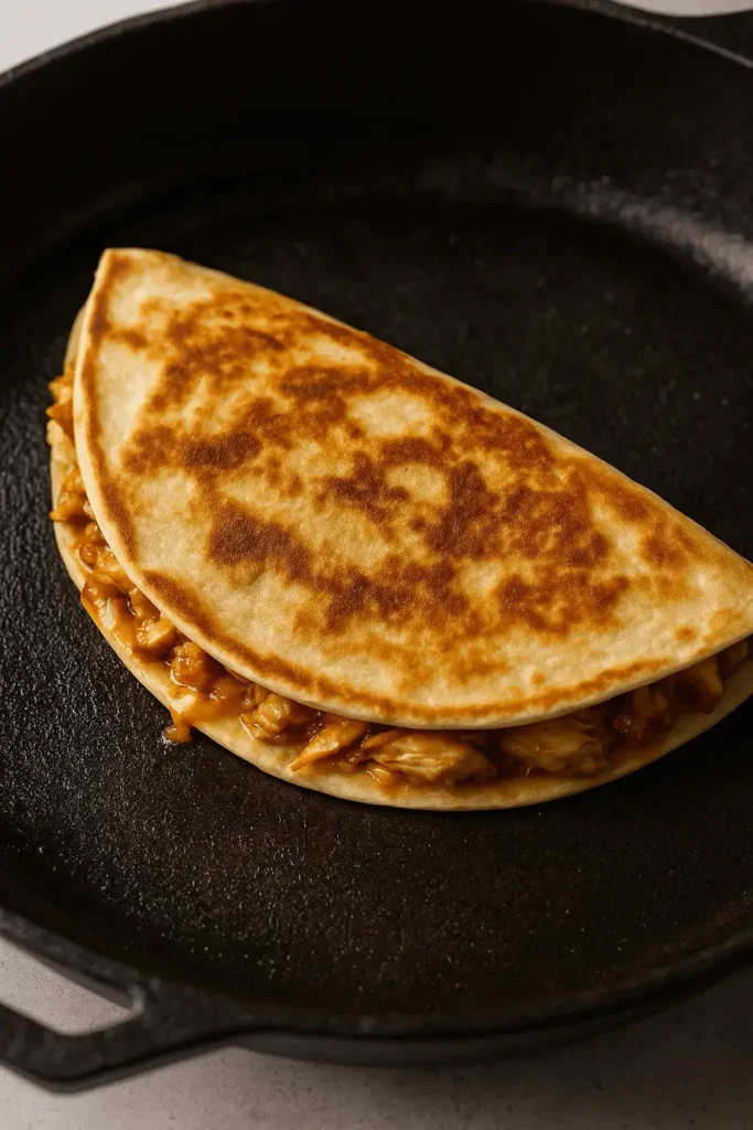 Chicken quesadilla recipe cooking in a skillet with a golden-brown tortilla and cheesy filling.
