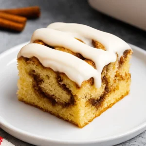 Single slice of cinnamon roll cake topped with smooth icing on a white plate.