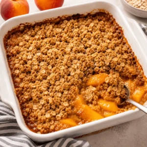 Peach Crisp with fresh peaches and a golden brown sugar oat topping in a white square baking dish.