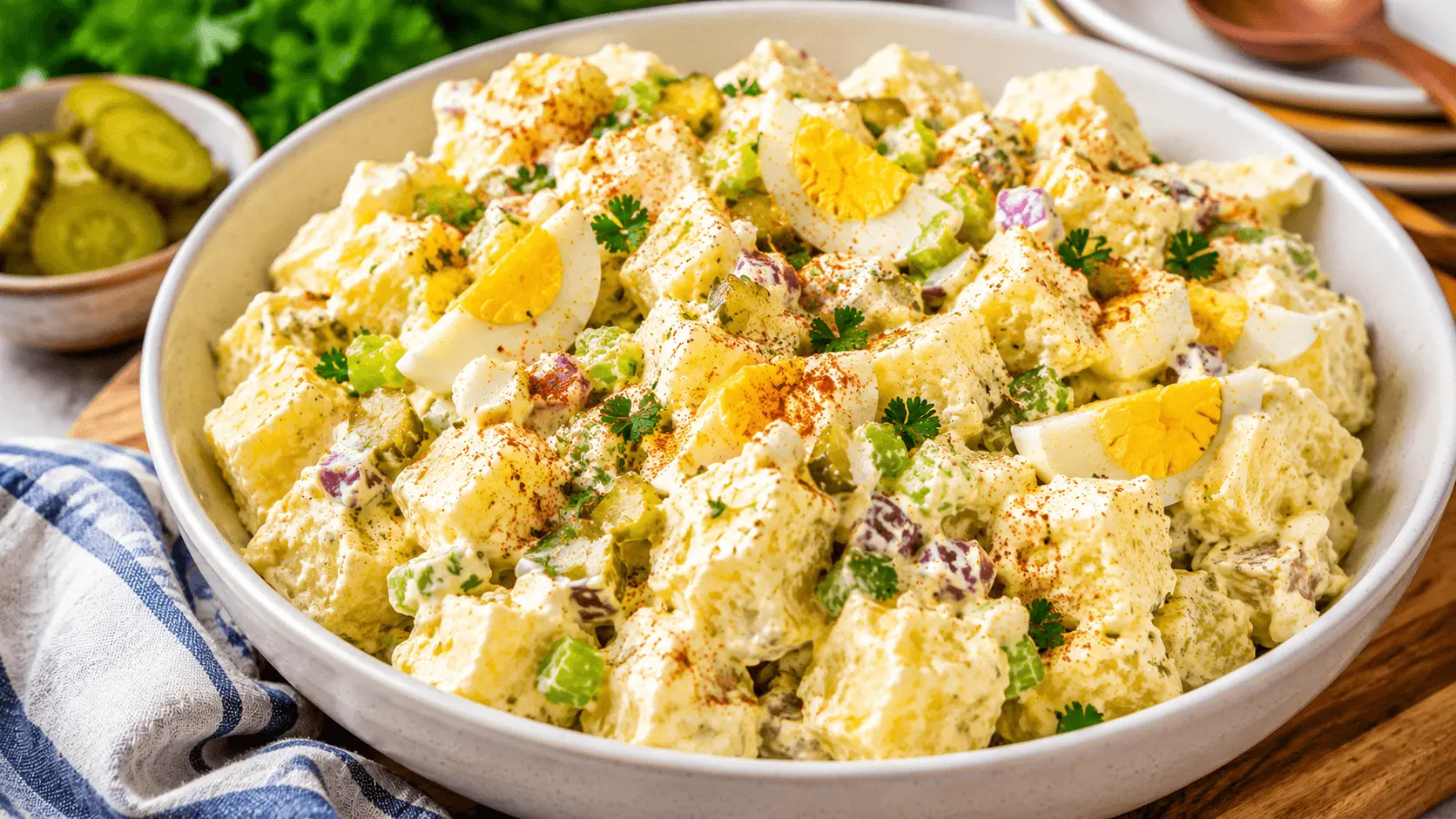 Potato Salad with Egg featuring creamy potato chunks, hard-boiled egg wedges, celery, red onion, dill pickles, parsley, and paprika in a white serving bowl.